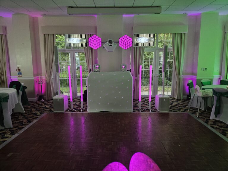 Disctilldawn Events DJ booth with white starlit front, pink uplighters and disco-ball wall decorations at a wedding reception
