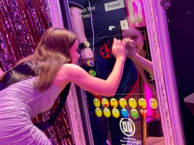 Magic Mirror photo booth in use at event with guest interacting and emoji graphics on the mirror display