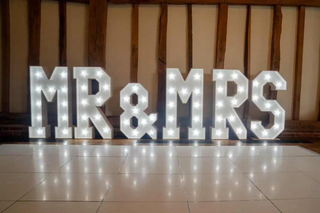 Large illuminated MR and MRS letters on white starlit dance floor in rustic barn wedding venue