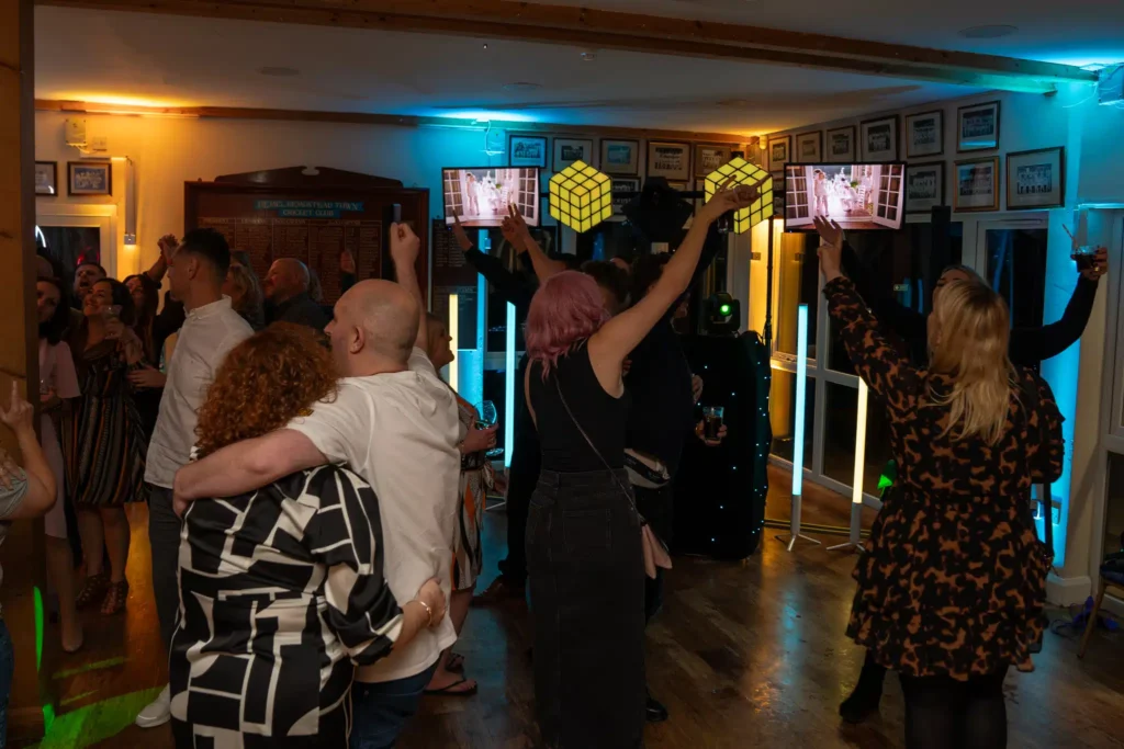 Wedding crowd celebrating with hands raised in ornate venue under blue and teal uplighting