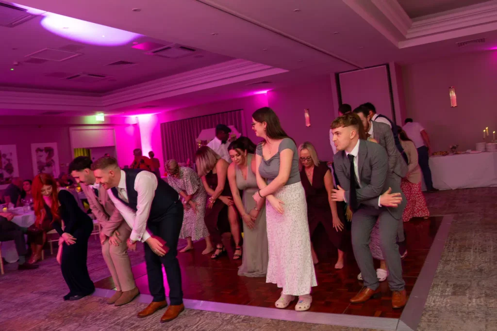 Wedding reception dance floor with bride, groom and crowd dancing in pink lit classic ballroom