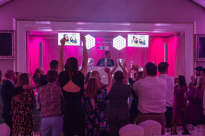Wedding party crowd dancing with photo booth and illuminated cube speakers in pink lit venue