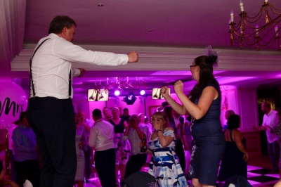 Wedding guests dancing energetically with pink uplighting and DJ photo booth setup behind