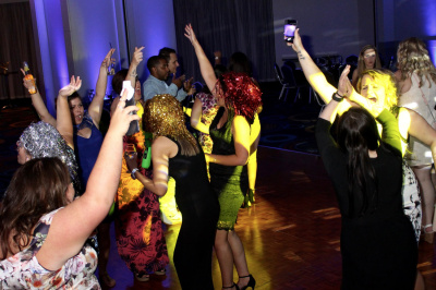 Party crowd celebrating with hands raised and woman in golden dress visible at energetic event