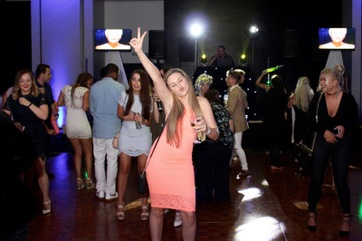 Birthday party celebration with woman in coral dress and crowd dancing under white spotlights