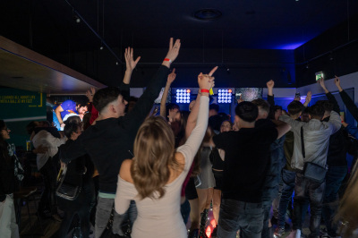 Birthday party crowd dancing under bright white spotlights with woman in coral dress in foreground