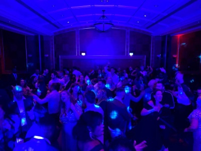 Wide shot of party crowd dancing in dim blue uplit ballroom venue at private event