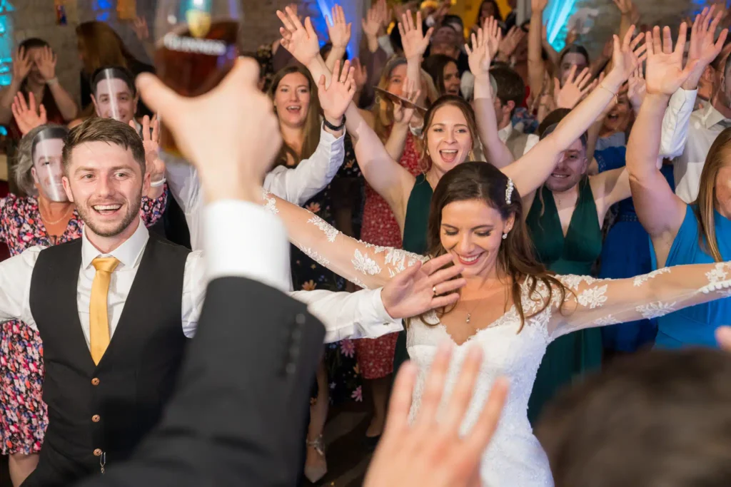 Wedding reception crowd cheering with hands raised celebrating with bride and groom on dance floor