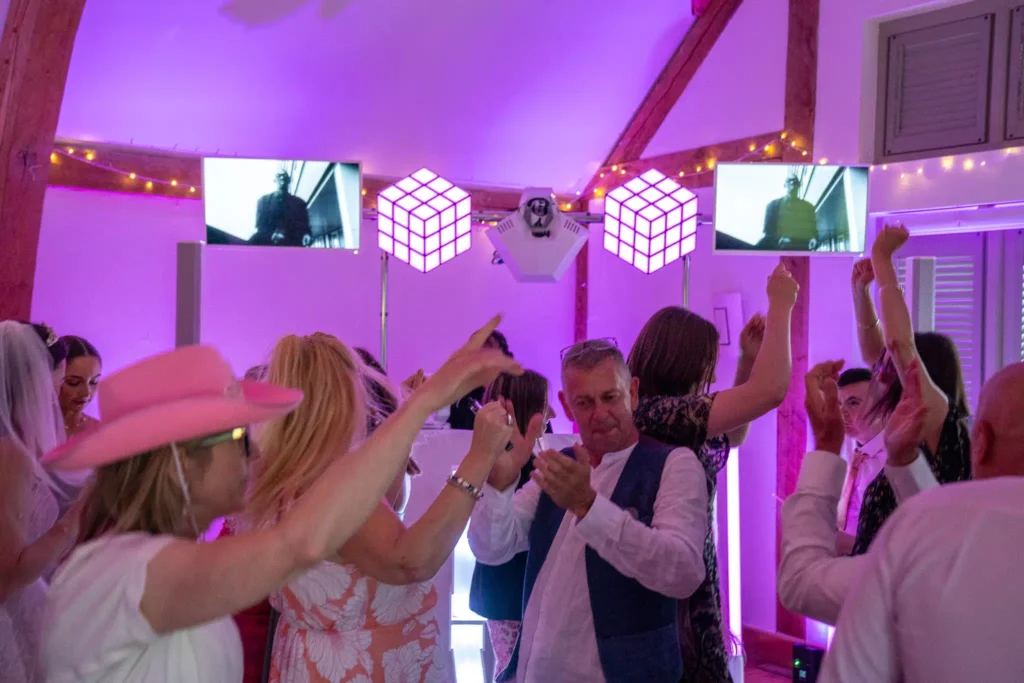 Themed wedding party with pink uplighting, illuminated cube speakers and fairy lights in barn venue