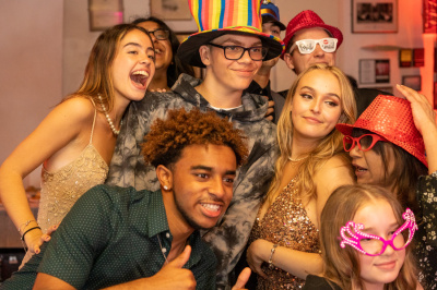 Group of friends posing for photo booth photo with rainbow hat fancy dress and party props