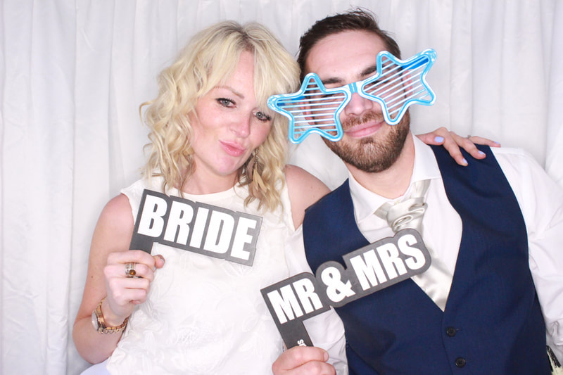 Bride and groom in a Disctilldawn Events wedding photo booth holding 'Bride' and 'Mr & Mrs' signs with novelty star sunglasses