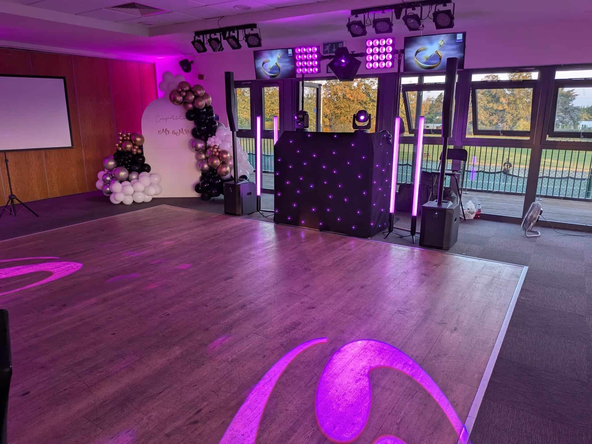 Disctilldawn premium disco DJ booth with pink uplighters, TV screens and balloon backdrop in a bright function room