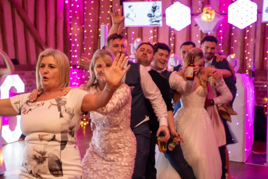 Wedding photo booth crowd at barn venue with pink uplighting, fairy lights and Magic Mirror booth