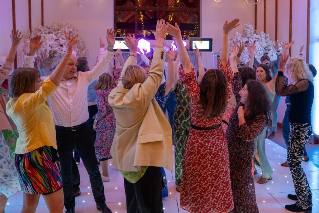 Wedding reception crowd dancing with hands raised under fairy lights and LED cube show