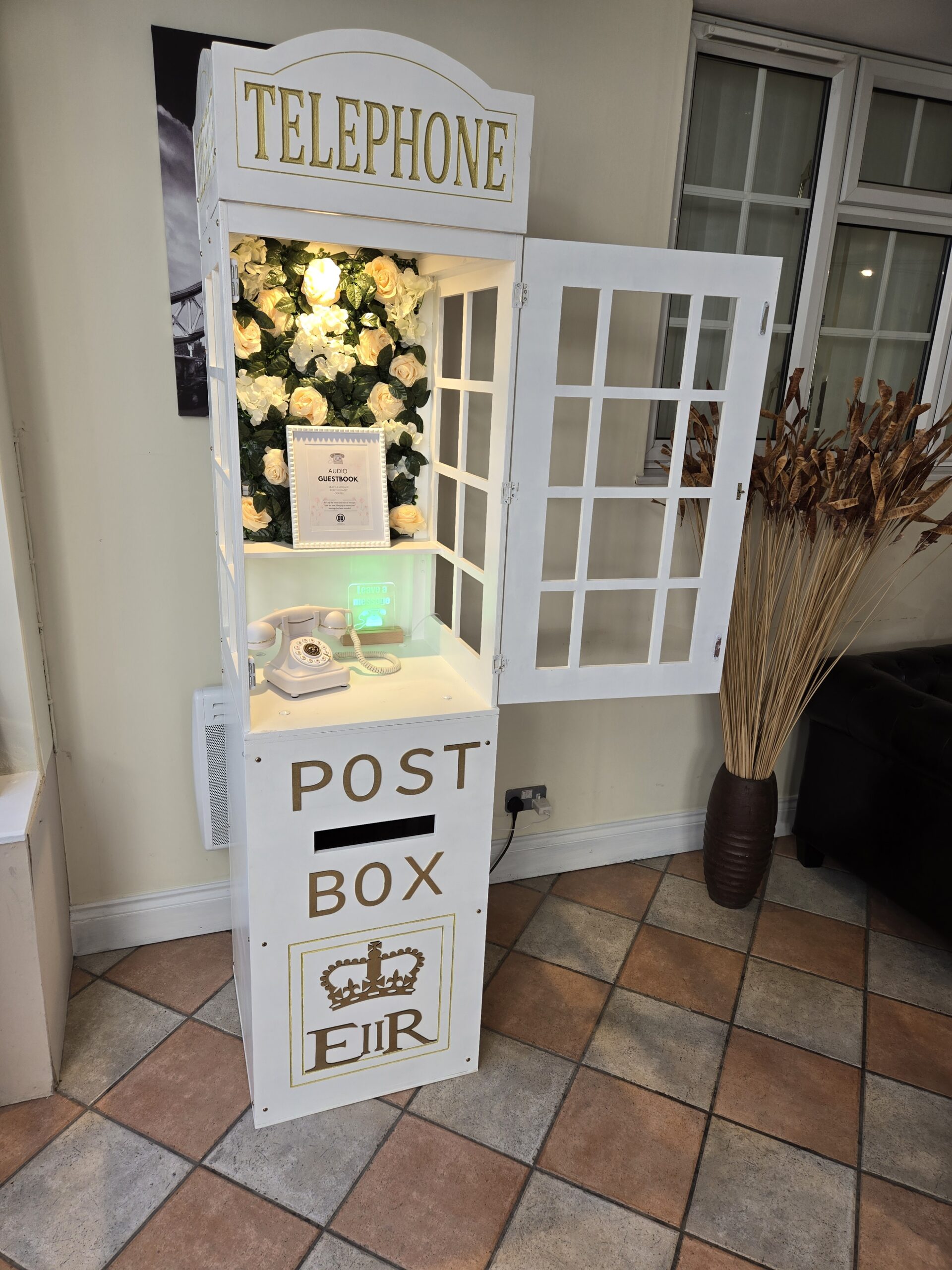 White audio guestbook telephone box with cream rose flower wall at a wedding