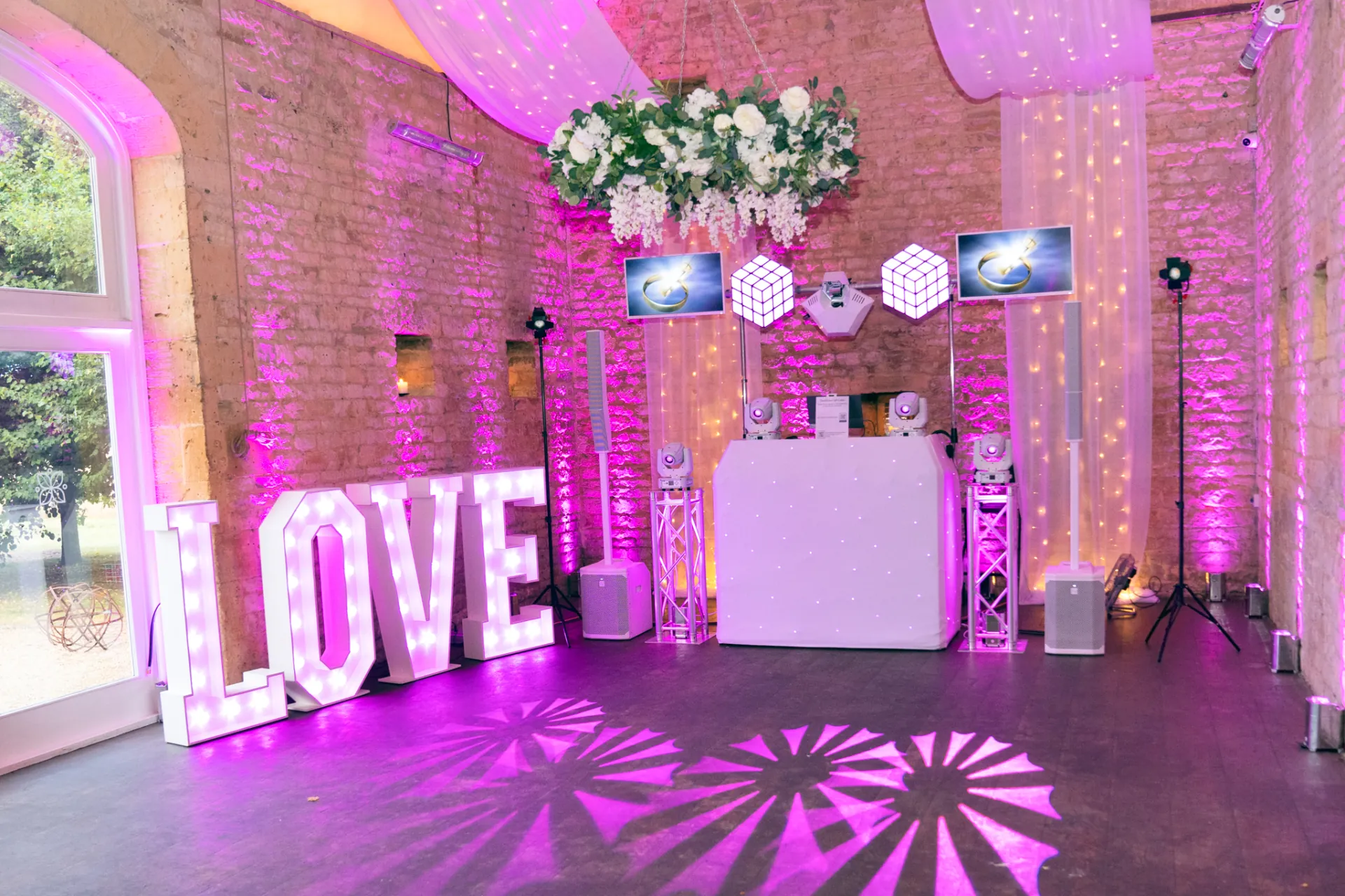 Light-up LOVE letters with white drape and pink uplighting at a wedding